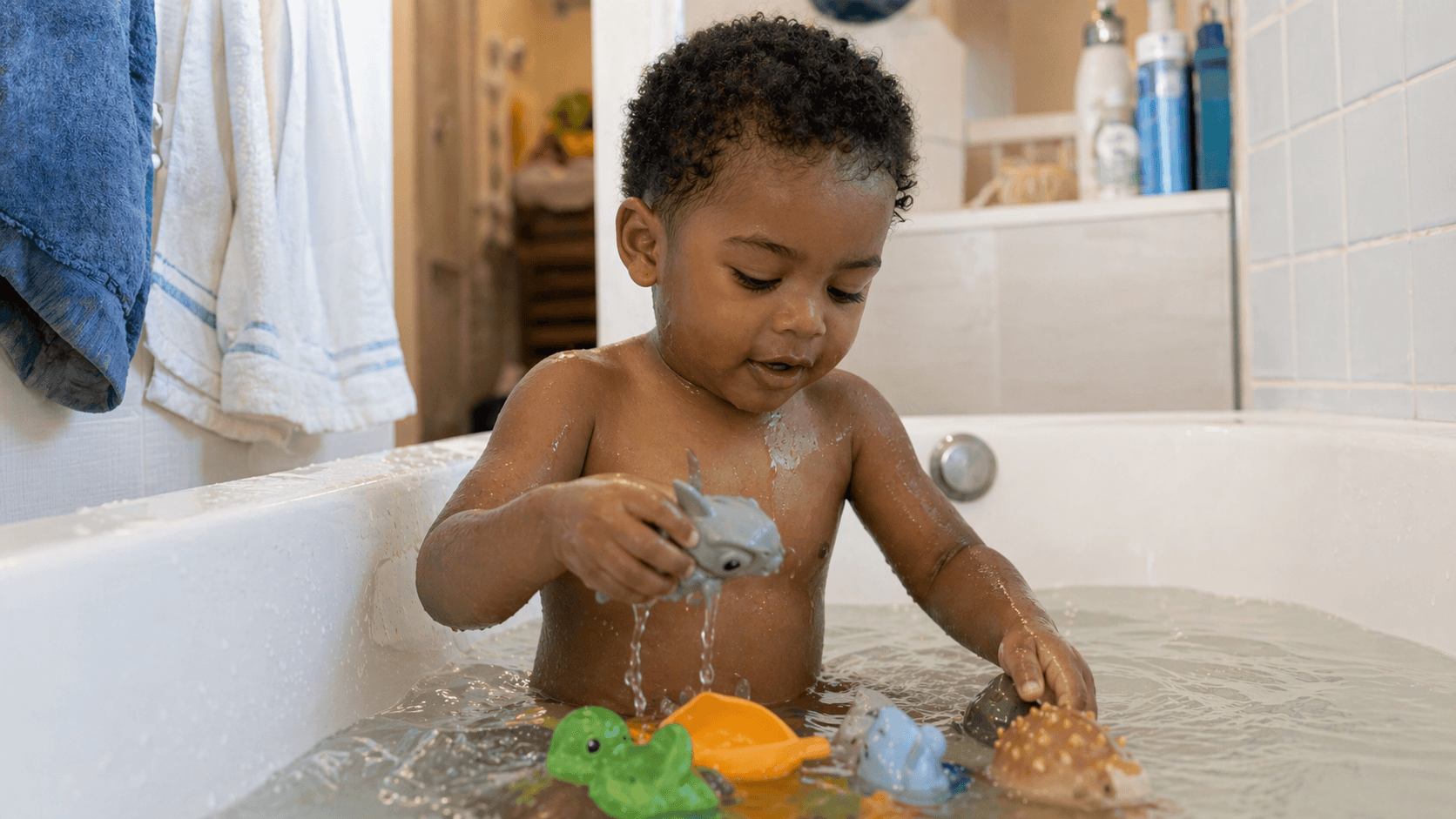 Toddler playing with water and toys at home in the bathtub on a hot day