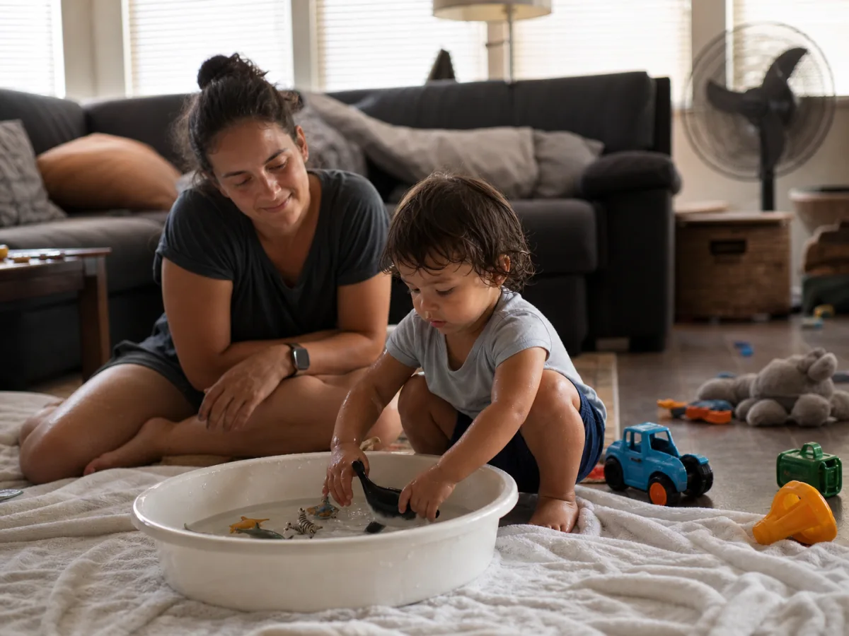 Toddler washing toy animals in a shallow basin in a cool living room