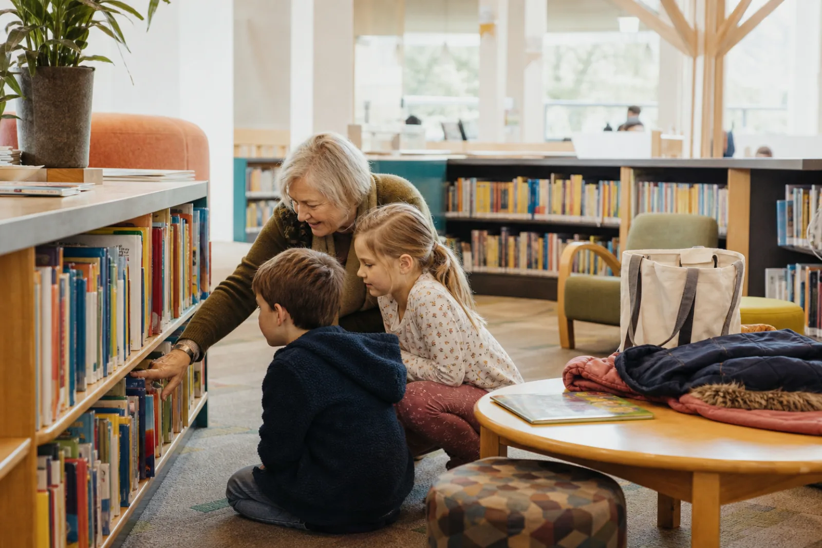 Grandmother and two children choosing books in a public library children's room