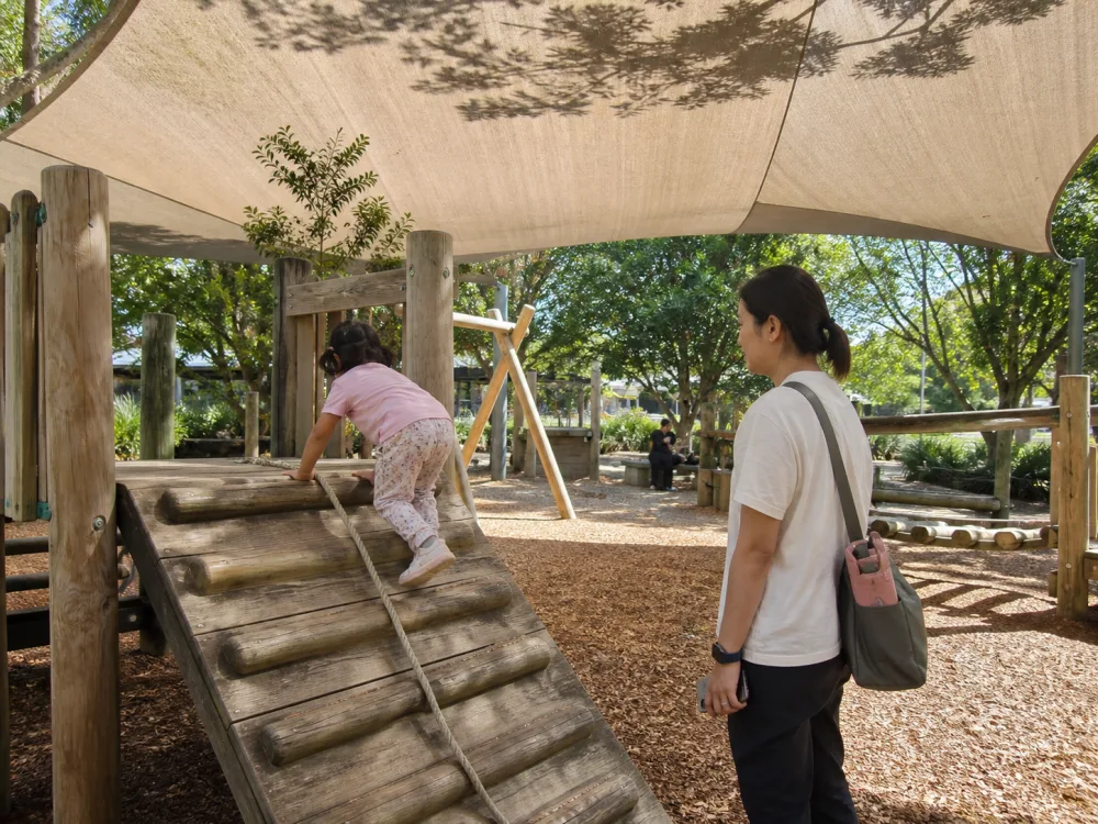 Child climbing on a wooden playground under broad shade sails
