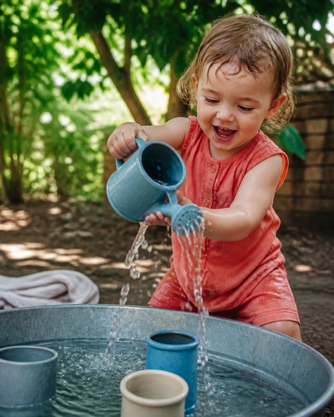 Toddler pouring water from a small watering can into a play tray