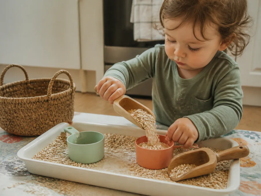 Toddler scooping oats in a simple homemade sensory tray