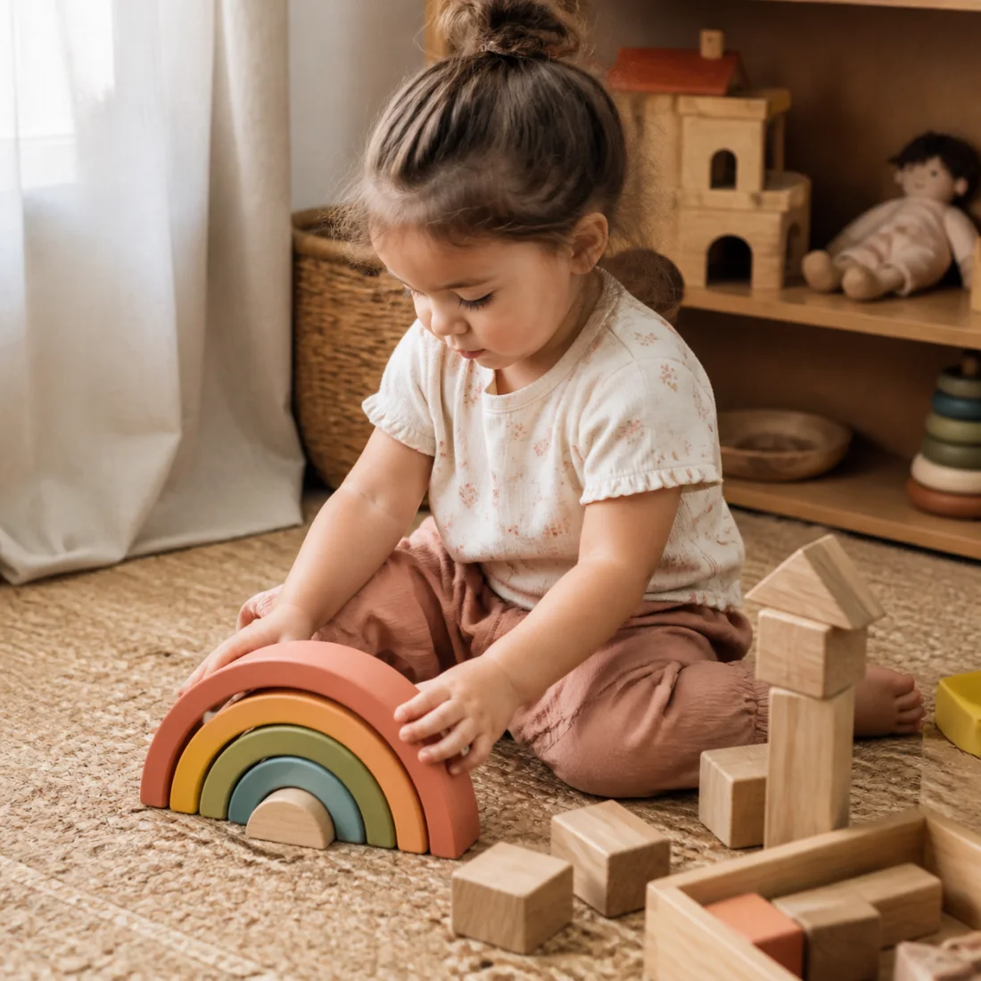 Two-year-old arranging a wooden rainbow and blocks on a rug