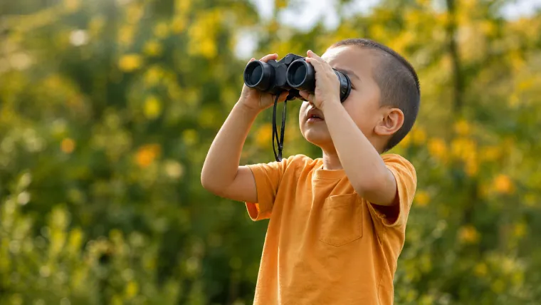 Child using binoculars outdoors while discovering something new